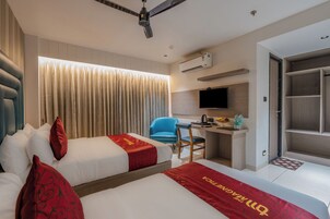 A hotel room with two beds, a desk, a chair, a television, and an air conditioning unit.