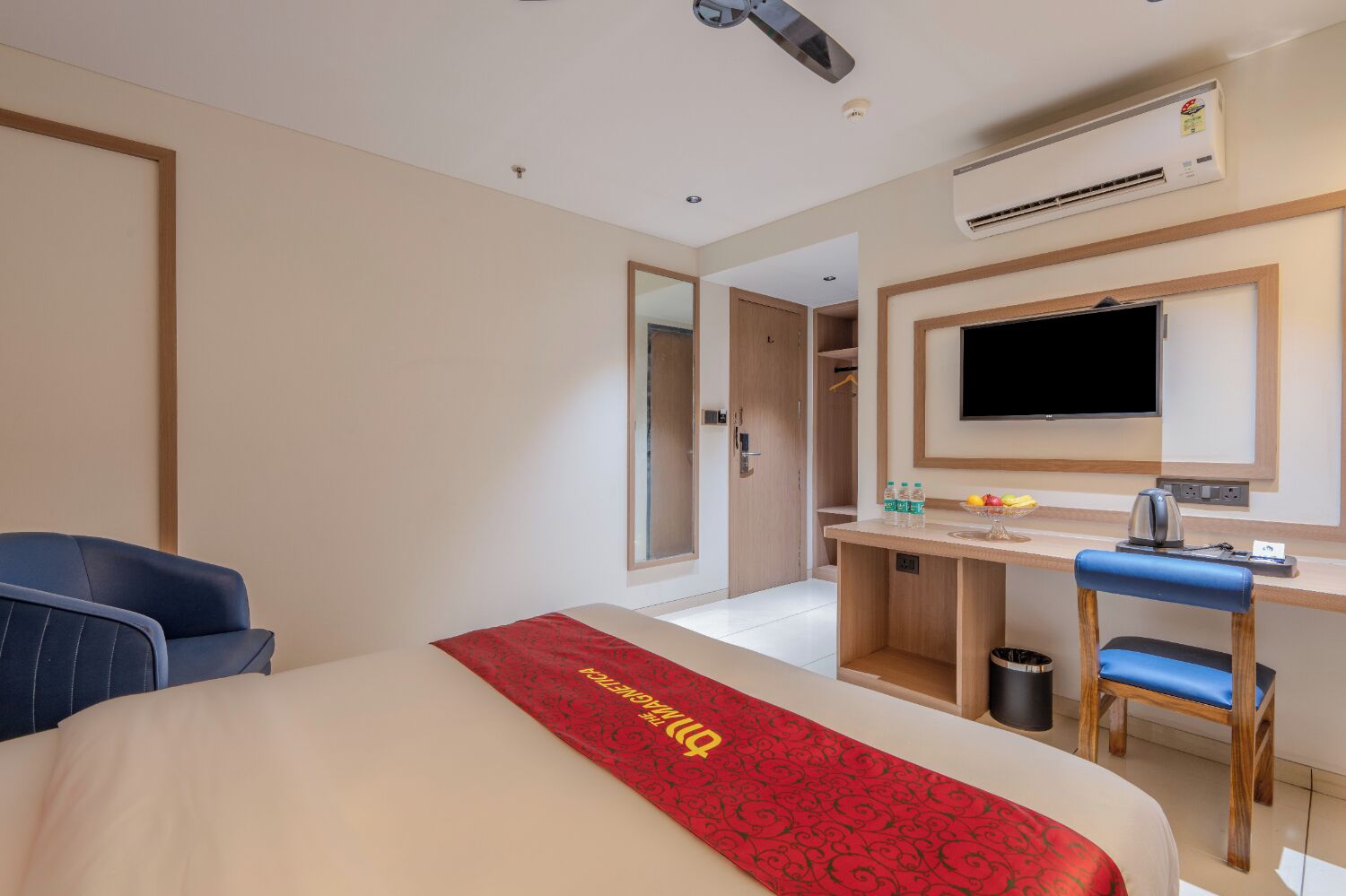 A hotel room with a bed, a desk, a chair, a TV, and an air conditioning unit.