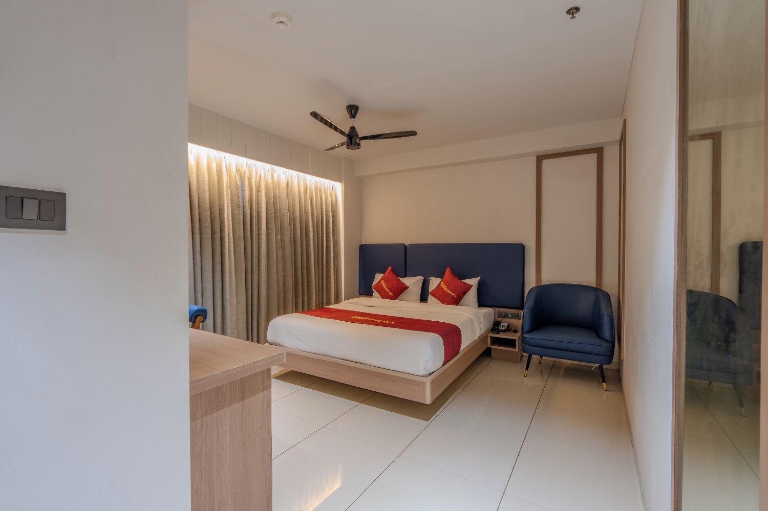 Una habitación de hotel moderna con cama, escritorio, silla, ventilador de techo y ventana con cortinas.