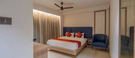 Una habitación de hotel moderna con cama, escritorio, silla, ventilador de techo y ventana con cortinas.