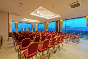 Un salón de conferencias con hileras de sillas rojas, ventanas amplias y una lámpara de araña moderna.