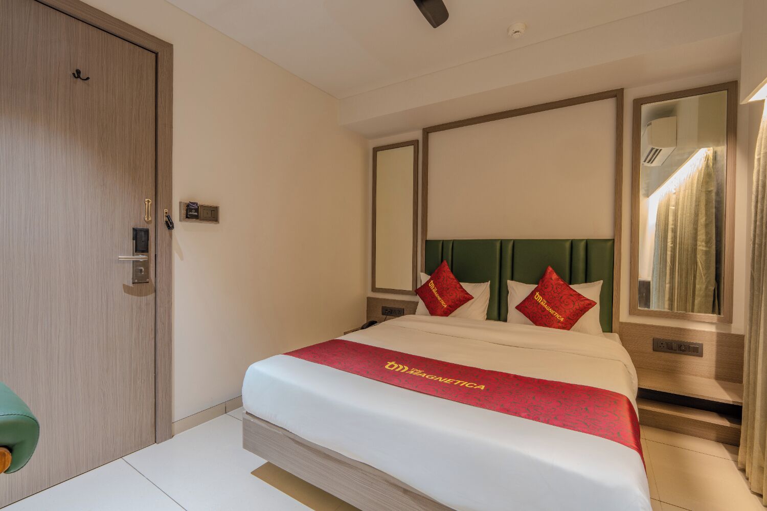 Habitación de hotel con cama, puerta, espejo y ventana con cortinas.