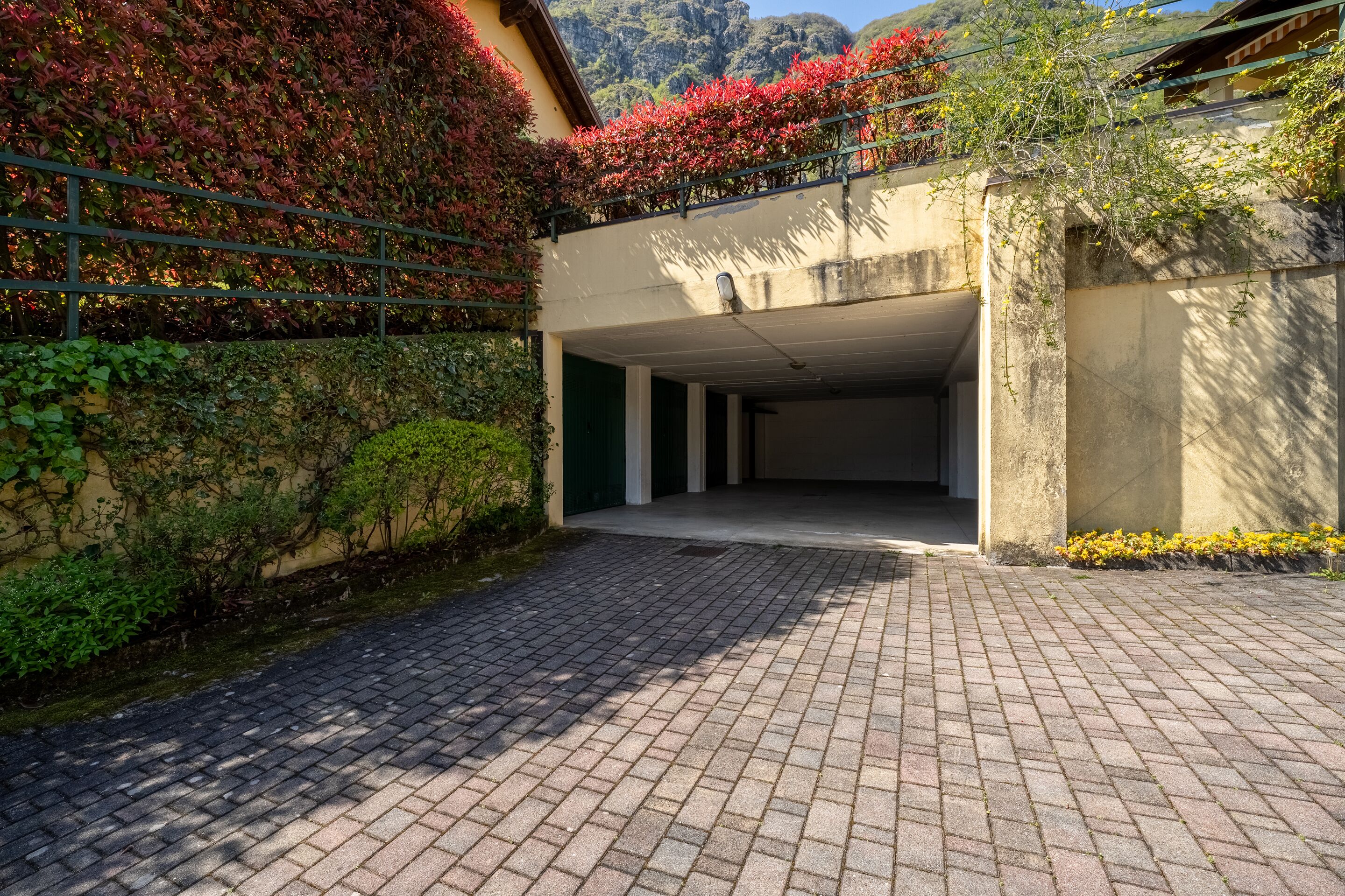 A paved driveway leading to a building with a covered entrance, surrounded by greenery and a mountainous backdrop.