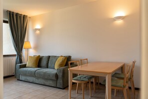 Ein Zimmer mit einer Couch, einem Tisch, Stühlen, einer Lampe und einer Wandleuchte.