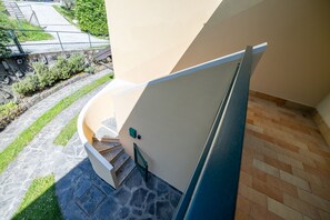 Eine Treppe mit Geländer führt zu einer Tür, der Boden ist mit Steinplatten ausgelegt und es gibt einen kleinen Gartenbereich mit Gras und Pflanzen.