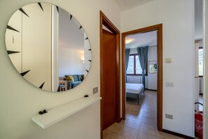 Ein Flur mit einem großen, runden Spiegel, einer Holztür, die zu einem Schlafzimmer führt, und einem weißen Regal.
