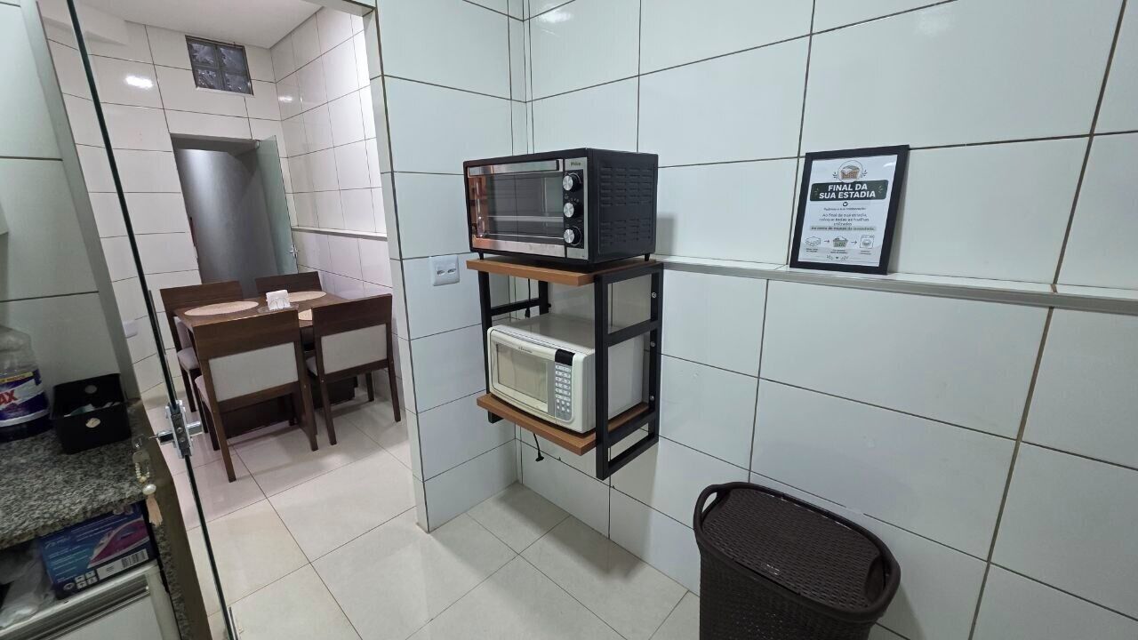 A small kitchenette with a microwave, a shelf unit, a trash bin, and a framed certificate on the wall.