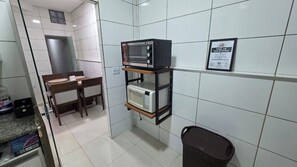 Een kleine kitchenette met een magnetron, een plankunit, een prullenbak en een lijst met een certificaat aan de muur.