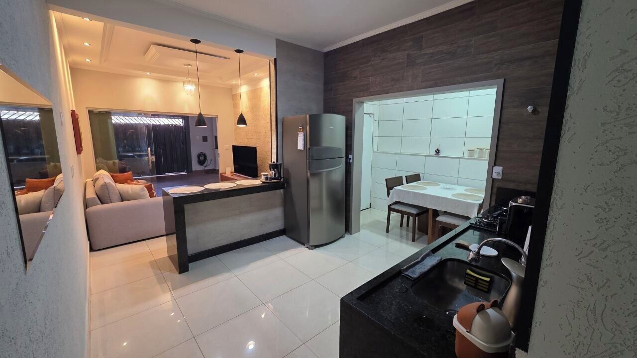 Una cocina moderna con una isla central, un comedor con mesa y sillas, y una sala de estar con sofá y televisor.