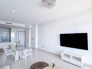 A modern living room with a glass dining table, white chairs, a flat-screen TV mounted on the wall, and a white console table. - Modern apartment with sea view - 4 guests (Benidorm)