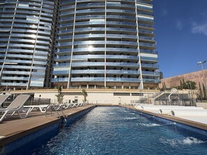 Un hôtel moderne doté d’un espace piscine, comprenant une grande piscine extérieure avec une terrasse en bois et des chaises longues.