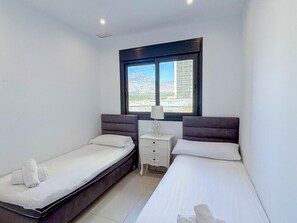 A hotel room with two beds, a nightstand, a window with a view of buildings and mountains, and a ceiling light. - Modern apartment with sea view - 4 guests (Benidorm)