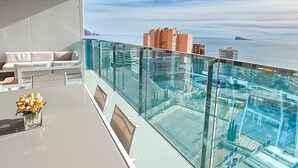 A balcony with a glass railing overlooking a pool and the sea. - Modern apartment with panoramic sea view (Benidorm)