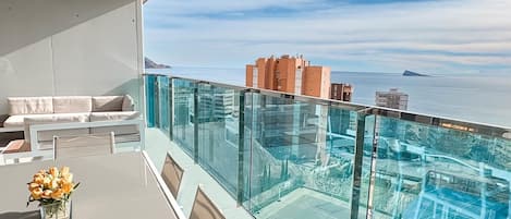 Balcón con barandilla de cristal que da a una piscina y al mar.