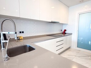 A modern kitchen with a stainless steel sink, a red kettle, and white cabinetry. - Modern apartment with panoramic sea view (Benidorm)