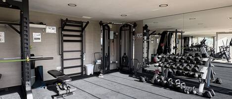 A gym with weightlifting equipment, benches, and dumbbells.
