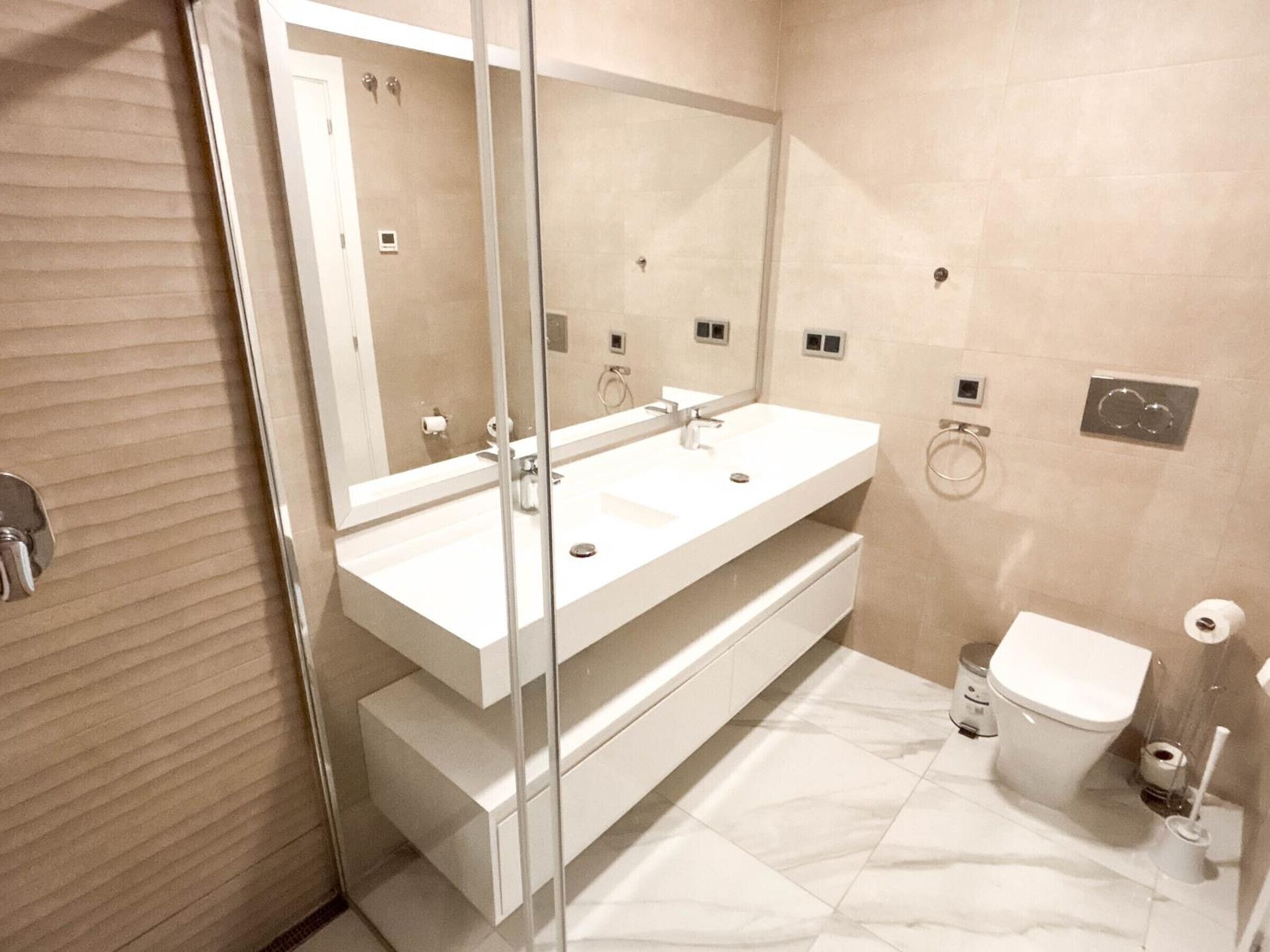 A modern bathroom with a glass shower enclosure, a double sink vanity, and a toilet.