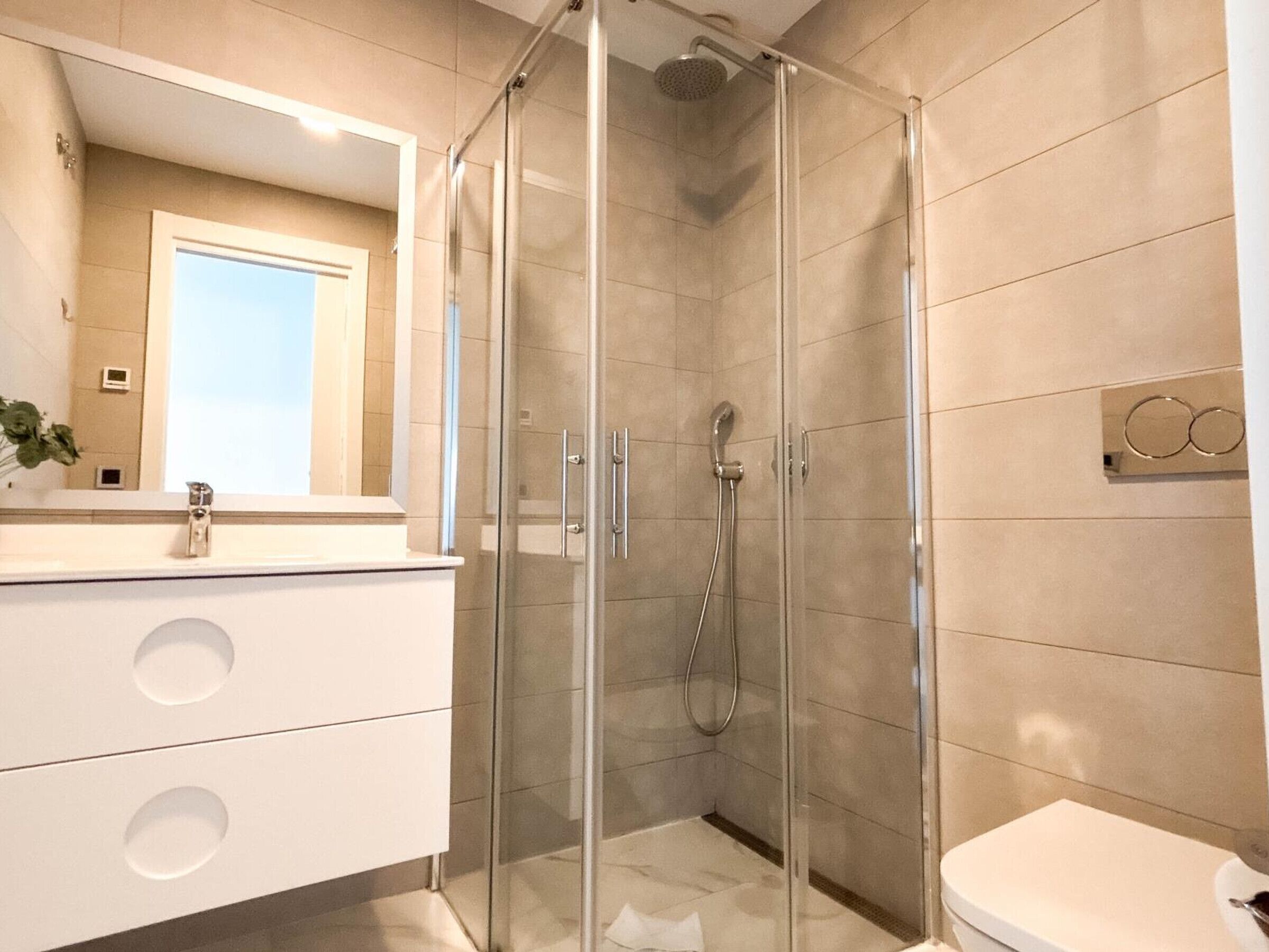 A modern bathroom with a glass-enclosed shower, a white sink, and a toilet.