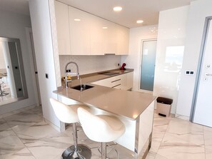 A modern kitchen with a central island, two bar stools, and a stainless steel sink. - Modern apartment with panoramic sea view (Benidorm)