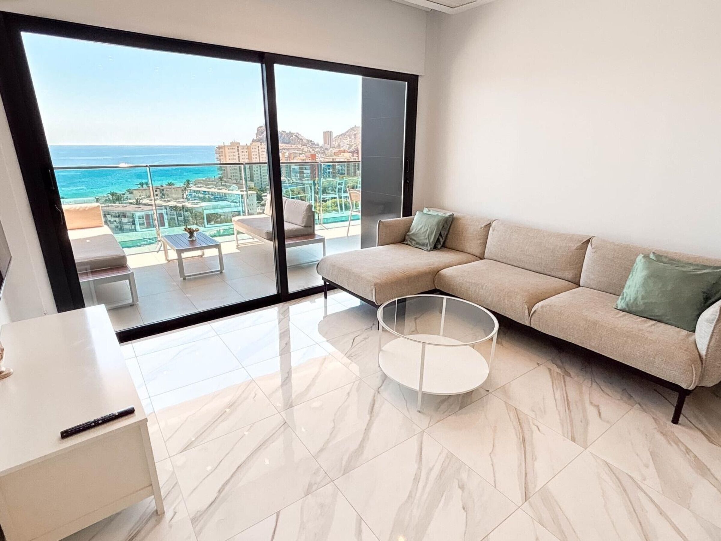 A modern living room with a large sliding glass door leading to a balcony overlooking a coastal cityscape.