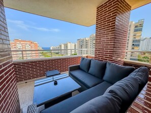 Ein Balkon mit einer Couch und einem kleinen Tisch, mit Blick auf eine Stadtlandschaft aus Gebäuden und einem klaren Himmel.