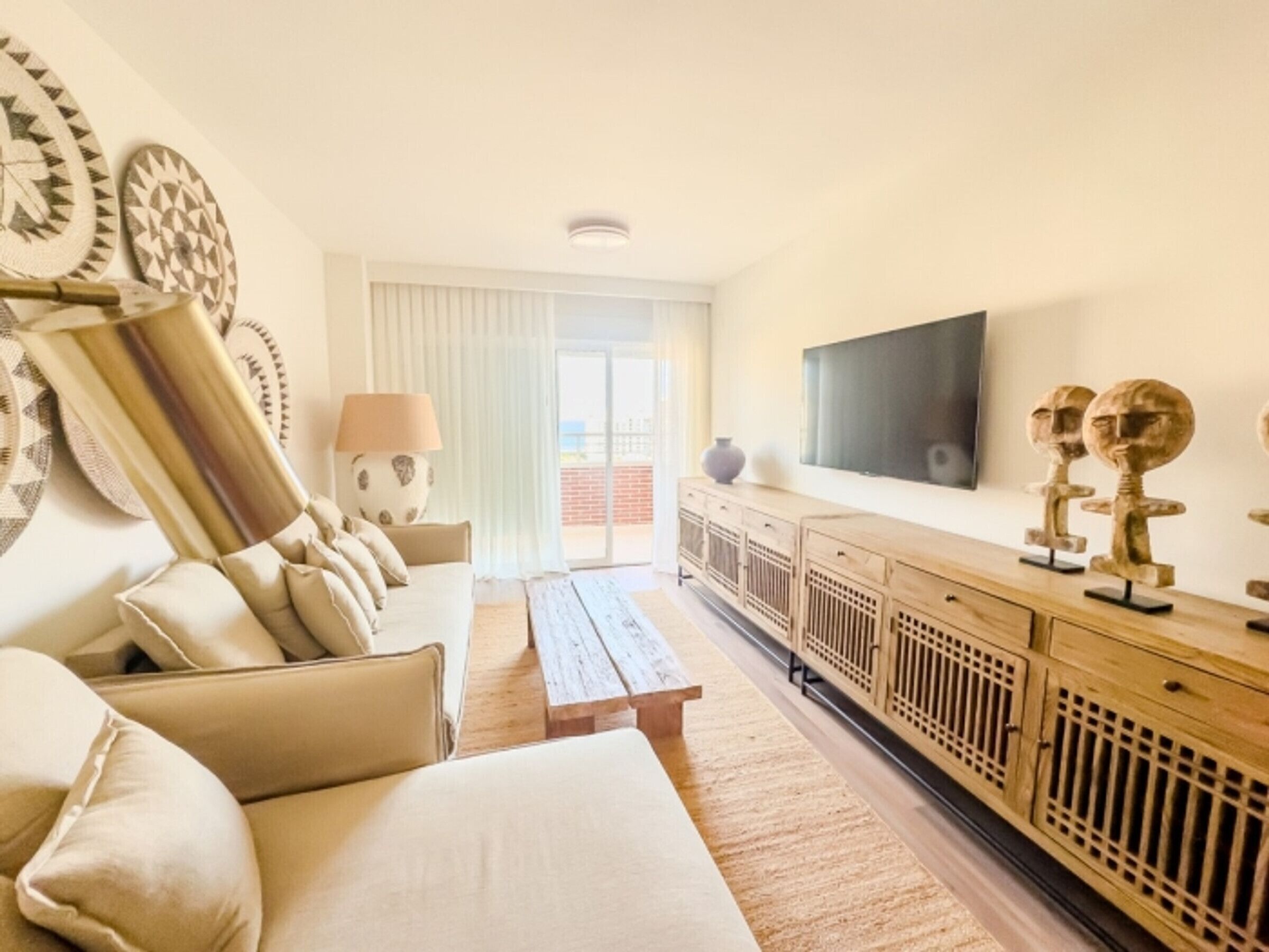 A modern living room with a sofa, a coffee table, a TV mounted on the wall, and decorative items on the sideboard.