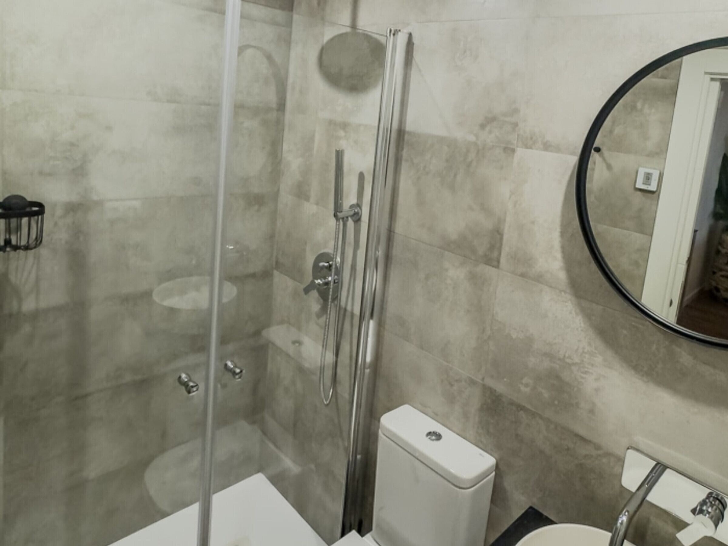 A bathroom with a glass-enclosed shower, a toilet, and a sink.