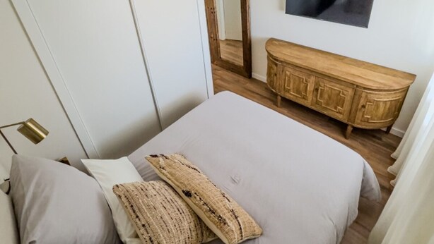 Ein Schlafzimmer mit einem Bett, einem Holzkleiderschrank, einem Spiegel und einem Fernseher an der Wand.