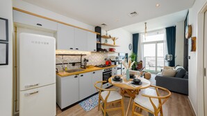 A compact kitchen with modern appliances, a dining area with a round table and chairs, and a living space with a sofa and a large window. - Boho-Chic 1BR w/ Pool | Dubai Hills (Dubai)