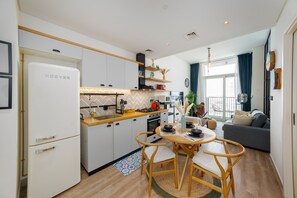 Eine kompakte Küche mit modernen Geräten, ein Essbereich mit rundem Tisch und Stühlen sowie ein Wohnbereich mit einer Couch und einem großen Fenster.
