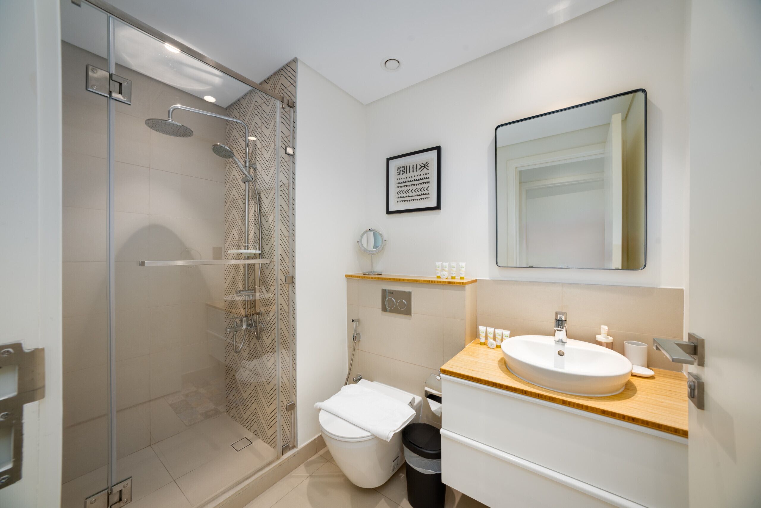 A modern bathroom with a glass-enclosed shower, a white toilet, a wooden vanity with a sink, and a mirror above the vanity.