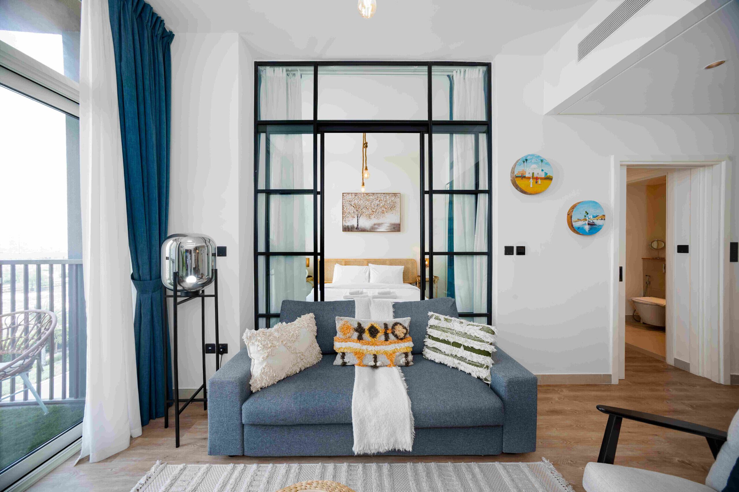 A modern living room with a grey sofa, a hanging light fixture, and a large window with curtains.