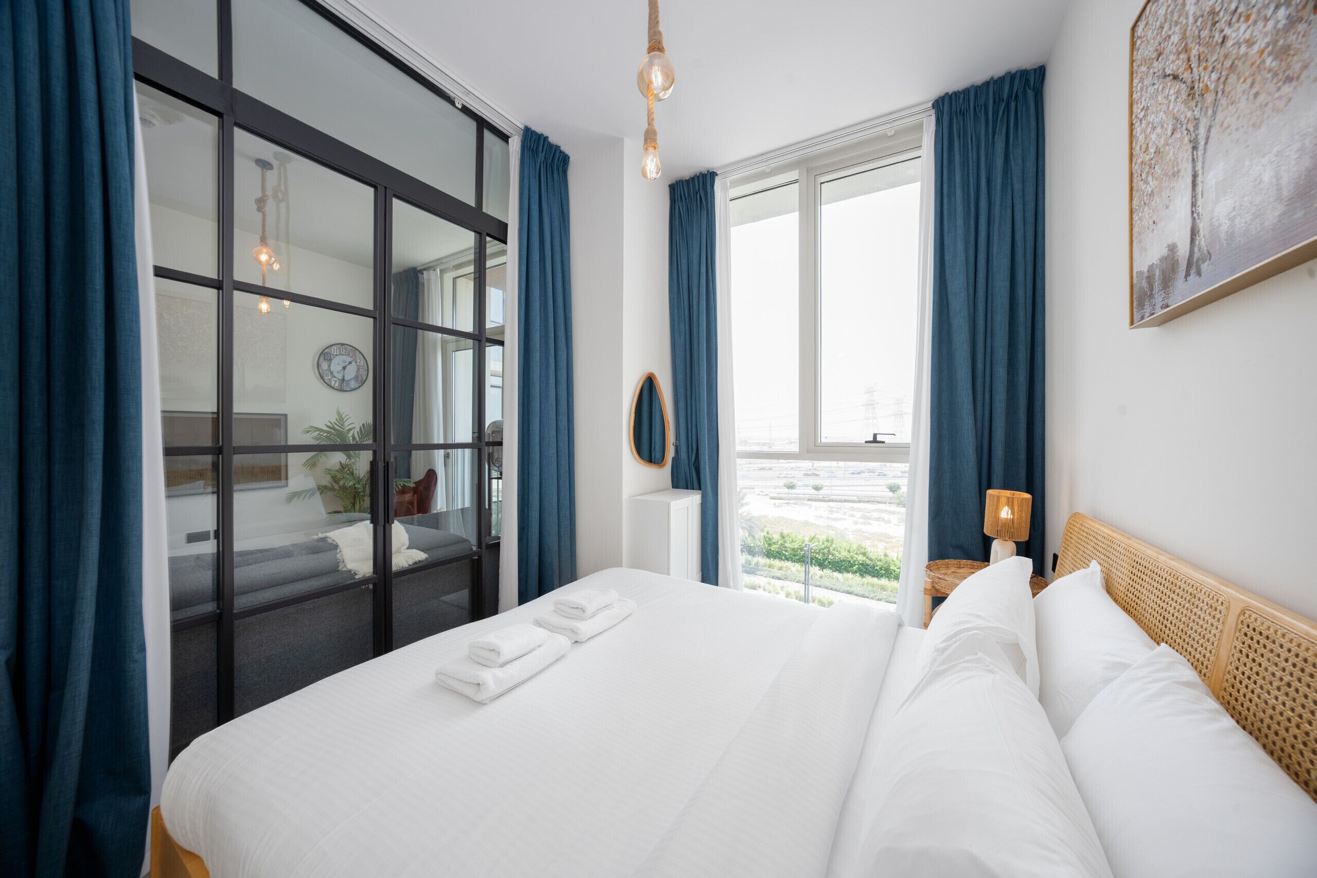 A hotel room with a large bed, a view through a glass door, a clock on the wall, and a window with curtains.