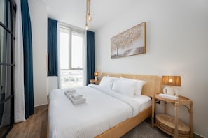 A hotel room with a large bed, a view of the city, and a painting on the wall. - Boho-Chic 1BR w/ Pool | Dubai Hills (Dubai)