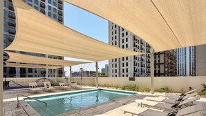A rooftop pool area with lounge chairs and a pool table, surrounded by high-rise buildings. - Boho-Chic 1BR w/ Pool | Dubai Hills (Dubai)