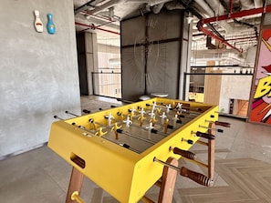 A foosball table in a room with a concrete floor, metal beams, and a large window. - Boho-Chic 1BR w/ Pool | Dubai Hills (Dubai)