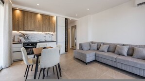 A modern living space with a kitchen, dining area, and a grey sofa. - Bella Vista Balcony 1BR Apartment (Vlorë)