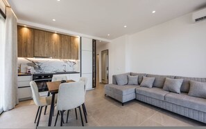 A modern living space with a kitchen, dining area, and a grey sofa. - Bella Vista Balcony 1BR Apartment (Vlorë)
