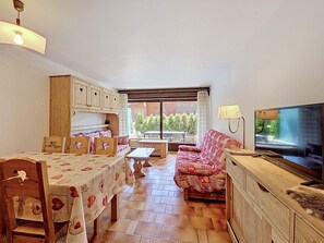 A cozy living room with a dining table, sofa, TV, and wooden cabinets. - Apartment with parking - 6 guests (La Clusaz)