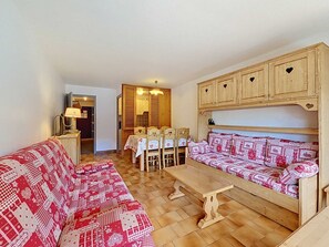 A cozy living room with a sofa, a wooden bench, a dining table with chairs, and a wooden cabinet with heart-shaped cutouts. - Apartment with parking - 6 guests (La Clusaz)