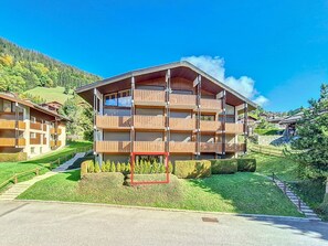 Ein mehrstöckiges Gebäude mit Balkonen, umgeben von viel Grün und blauem Himmel.