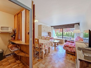 A cozy living space with a dining area, a sofa, a television, and a kitchen with wooden cabinets. - Apartment with parking - 6 guests (La Clusaz)