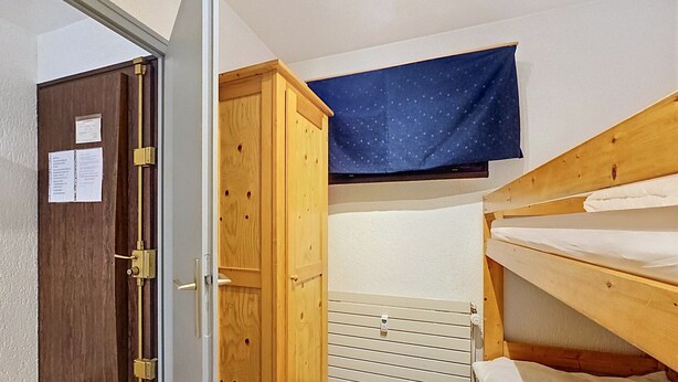Una habitación pequeña y funcional con un armario de madera, una cama litera y piso a cuadros.
