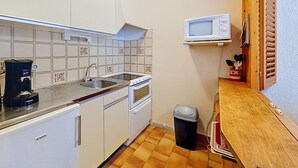 Cocina compacta con alacenas blancas, un lavamanos, cafetera, microondas y un cubo de basura.
