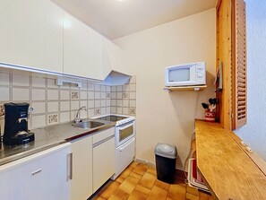 Eine kleine Küche mit weißen Schränken, einem Spülbecken, einer Kaffeemaschine, einer Mikrowelle und einem Mülleimer.