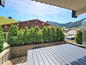 Ein Sitzbereich im Freien mit Tisch und Stühlen, einem Holzzaun und Blick auf einen Berg sowie Gebäude im Hintergrund.