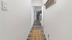 Um corredor com piso de madeira, paredes brancas, um tapete e uma placa emoldurada.