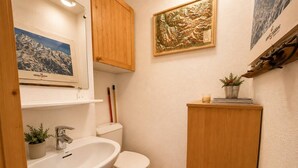 A bathroom with a sink, toilet, wooden cabinet, and a framed map on the wall. - Spacious duplex, mountain view - 5 guests (Méribel)