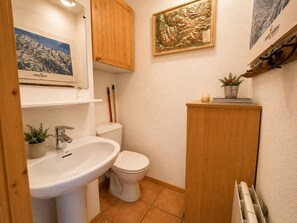 A bathroom with a sink, toilet, wooden cabinet, and a framed map on the wall. - Spacious duplex, mountain view - 5 guests (Méribel)