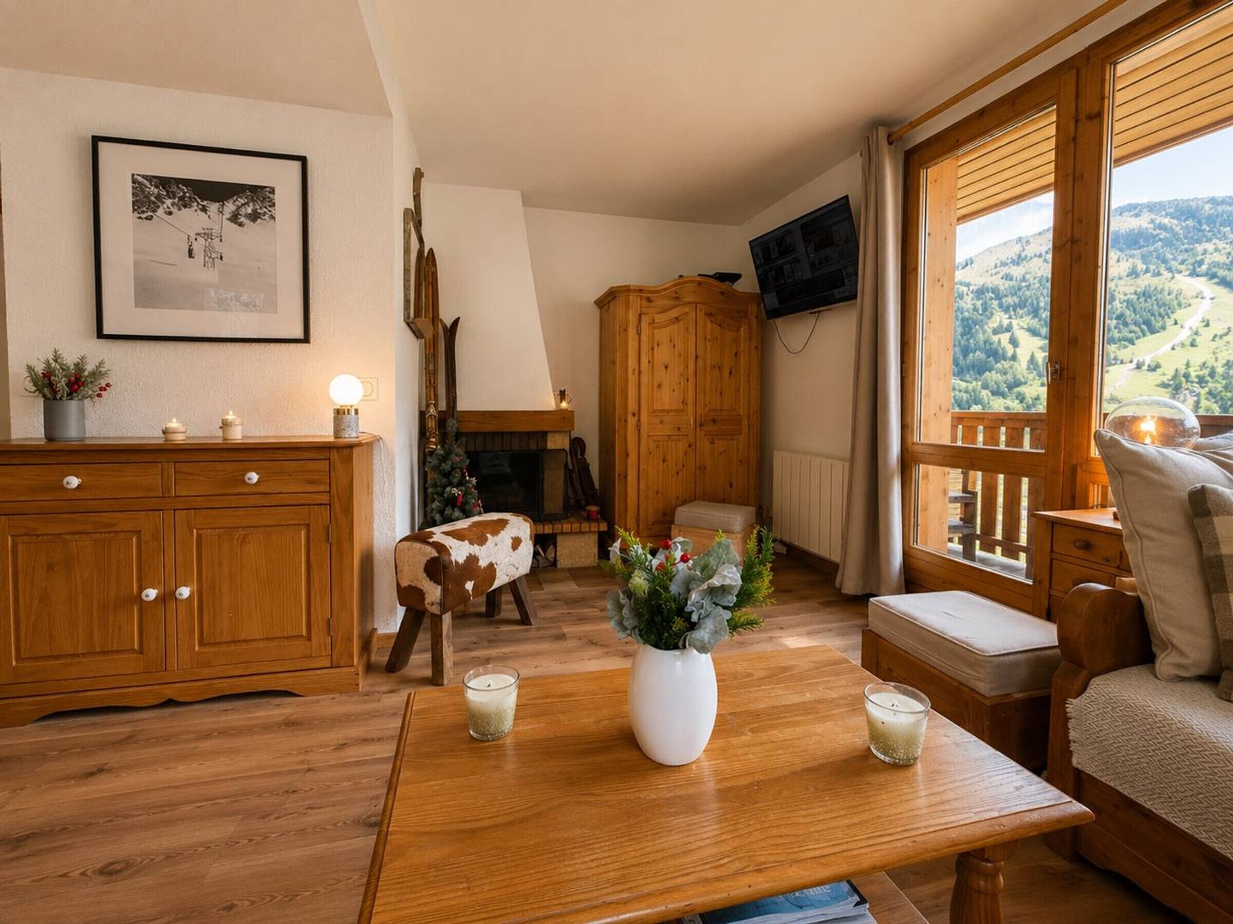 Un salon chaleureux avec un meuble en bois, une cheminée, un téléviseur fixé au mur et une vue sur l’extérieur grâce à de grandes fenêtres.